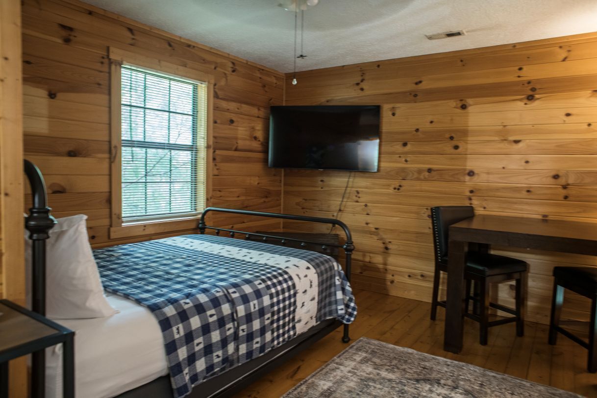 A wooden-paneled room with a bed, a desk, and a TV mounted on the wall.