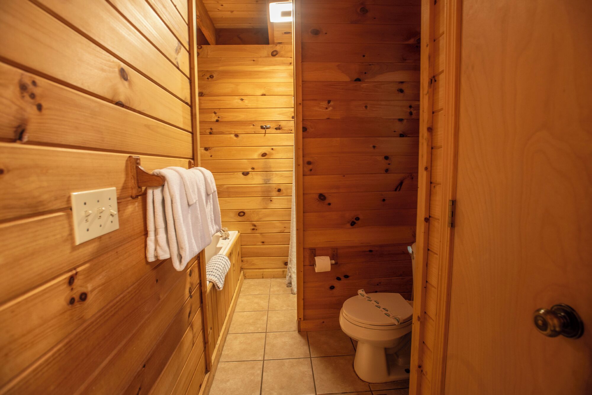 A wooden cabin bathroom with a toilet, a towel rack, and a small sink.