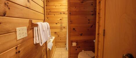 A wooden cabin bathroom with a toilet, a towel rack, and a small sink.