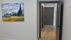 A hallway with a painting of a landscape, a door leading to a room, and a carpeted floor.