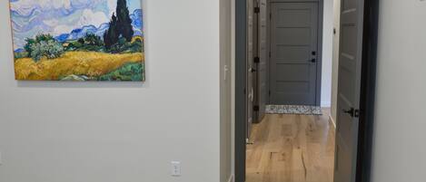 A hallway with a painting of a landscape, a door leading to a room, and a carpeted floor.