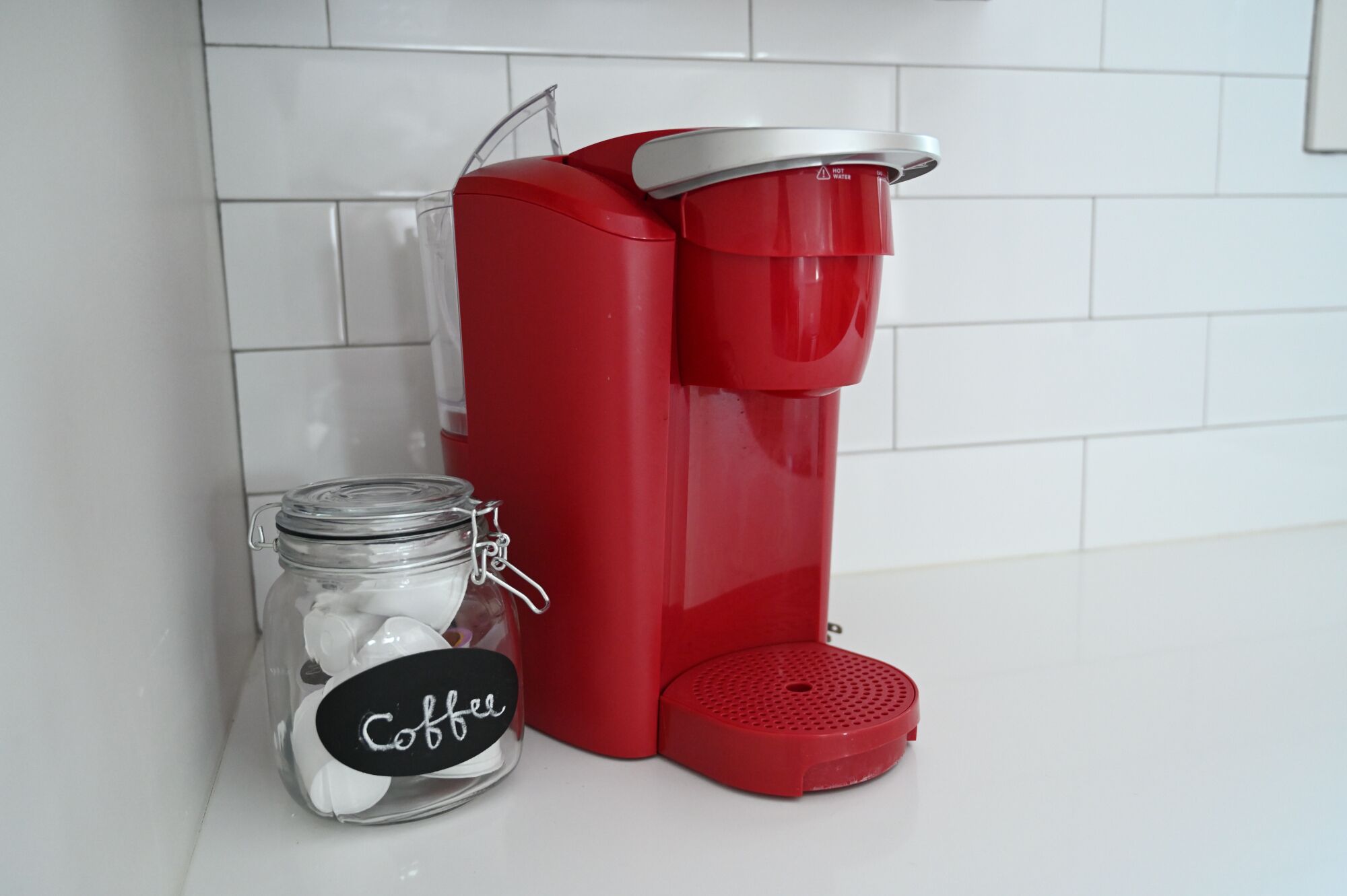 A red coffee maker next to a glass jar labeled "Coffee" on a white countertop.
