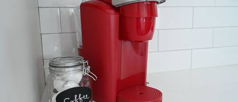 A red coffee maker next to a glass jar labeled "Coffee" on a white countertop.