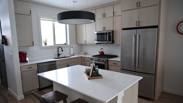 A modern kitchen with a central island, stainless steel appliances, and light wood cabinetry.