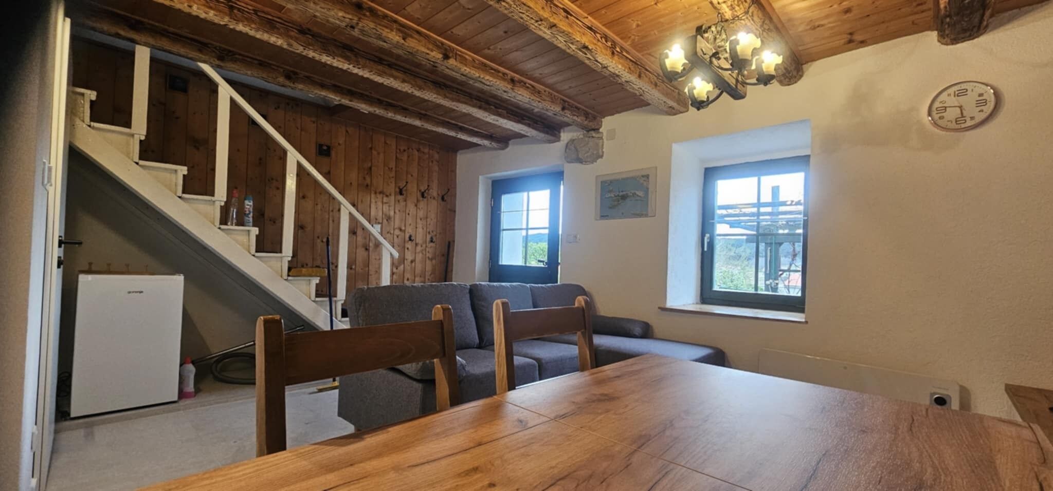 Ein gemütliches Zimmer mit einem Holzesstisch, einer Couch und einer Treppe, die in eine obere Ebene führt.