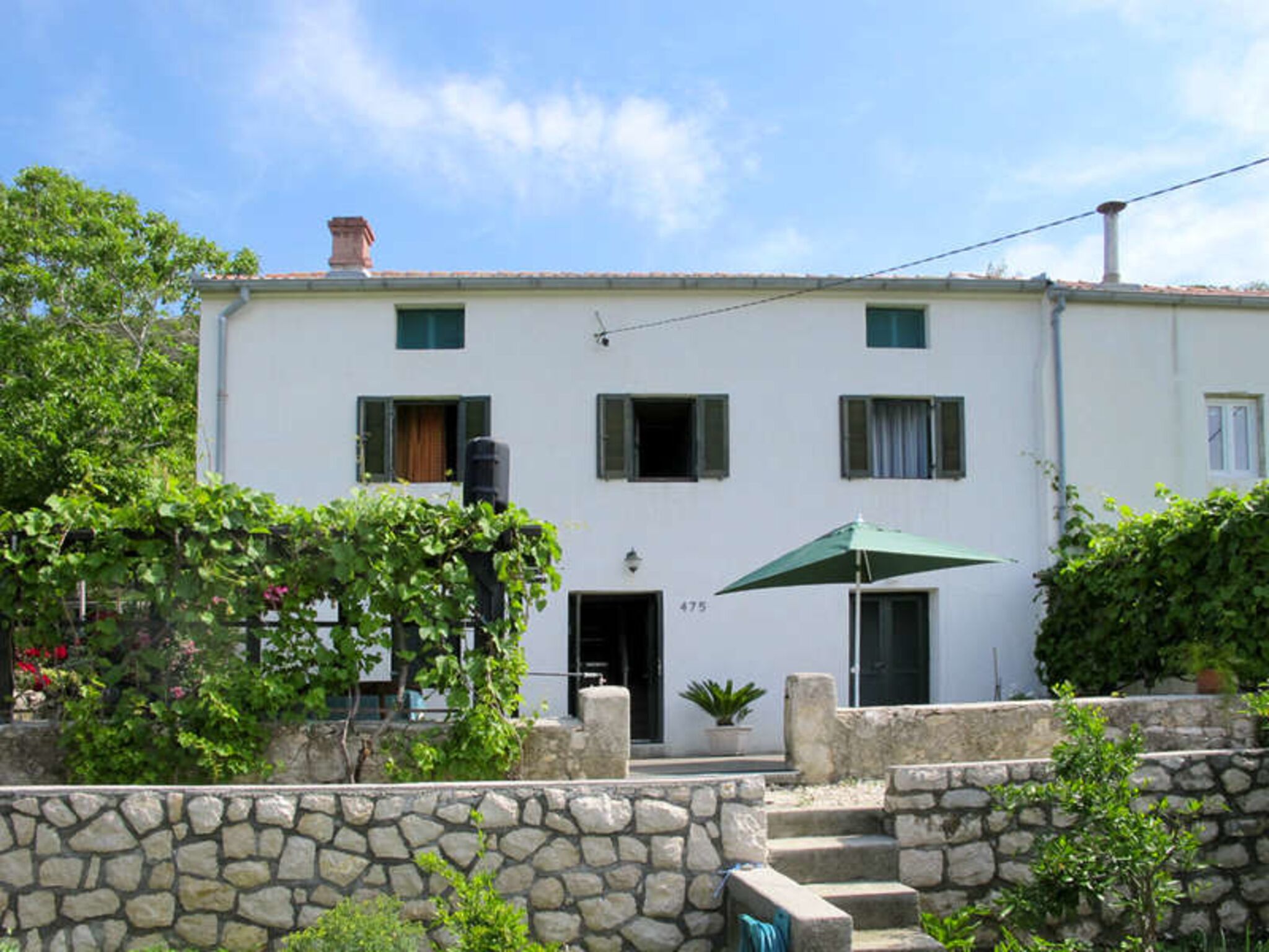 A two-story building with a stone wall in front, a green umbrella, and a potted plant.