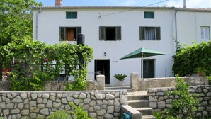 A two-story building with a stone wall in front, a green umbrella, and a potted plant. - Vacation House Viskic (Rab)