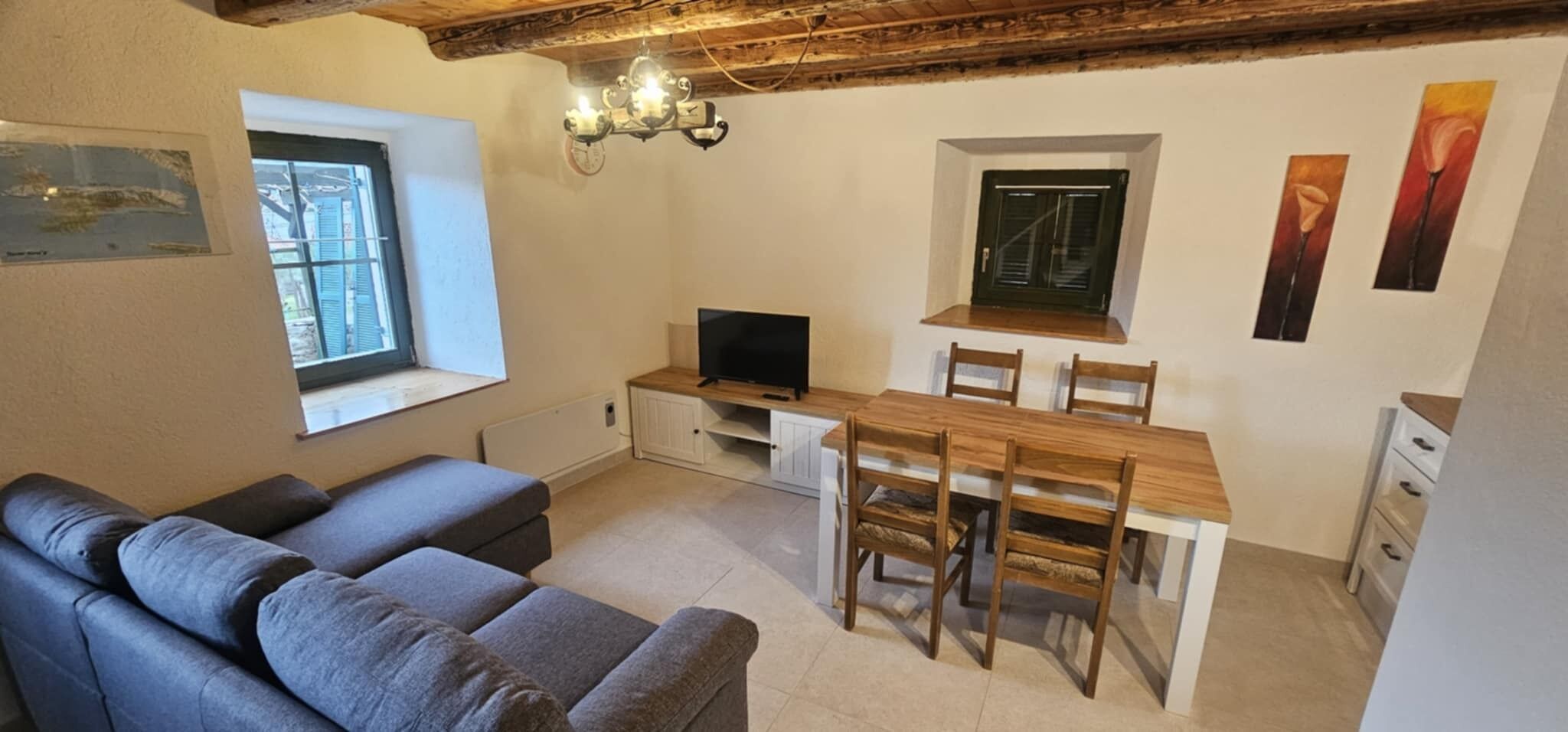 A compact living space with a sofa, a dining table with chairs, a TV, a window, and a door.