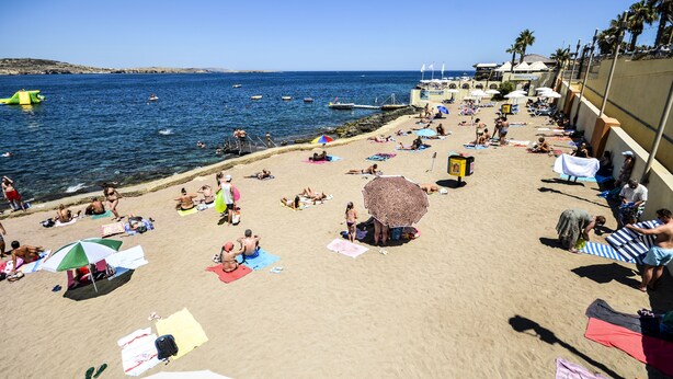 A beach with people sunbathing and swimming, umbrellas, and a clear blue sky. - Getawaysmalta - Seashells Apartment 11 With Terrace and Sea Views in Bugibba (St. Paul's Bay)