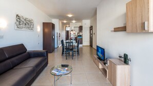 A modern living room with a sofa, a glass coffee table, and a flat-screen TV. - Getawaysmalta - Seashells Apartment 11 With Terrace and Sea Views in Bugibba (St. Paul's Bay)