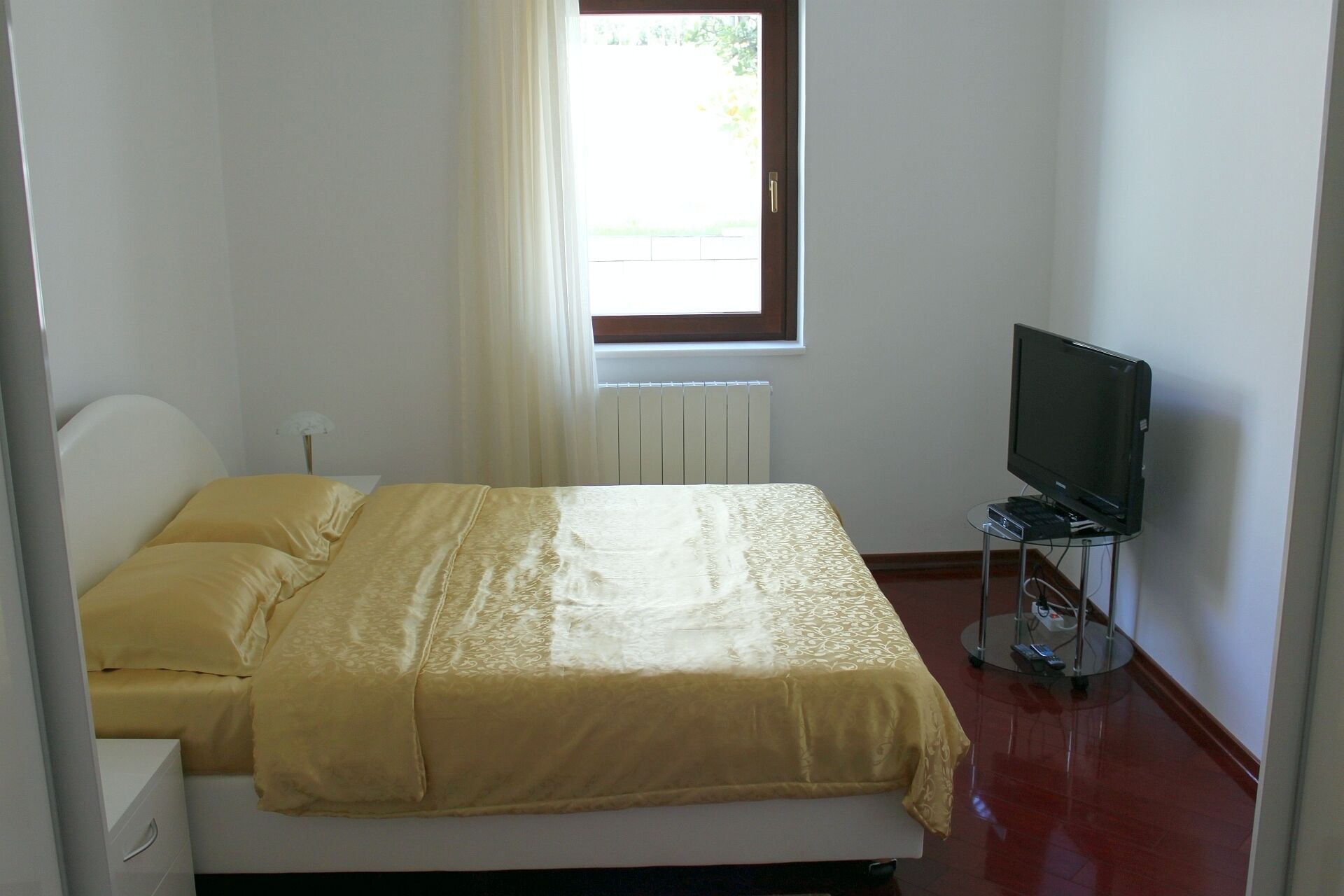 Un dormitorio con cama, televisor sobre un mueble bajo y ventana con cortinas.