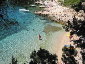 A beach with clear water, rocky shore, and people sunbathing.