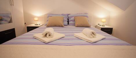 A neatly made bed with striped bedding and two pillows, two bedside lamps, and a folded towel on each side.