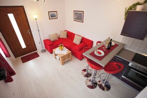 A compact living space with a red sofa, a small dining table, a kitchen area with a stove, and a bar stool. - Superior Apartment in Stari Grad (Stari Grad)
