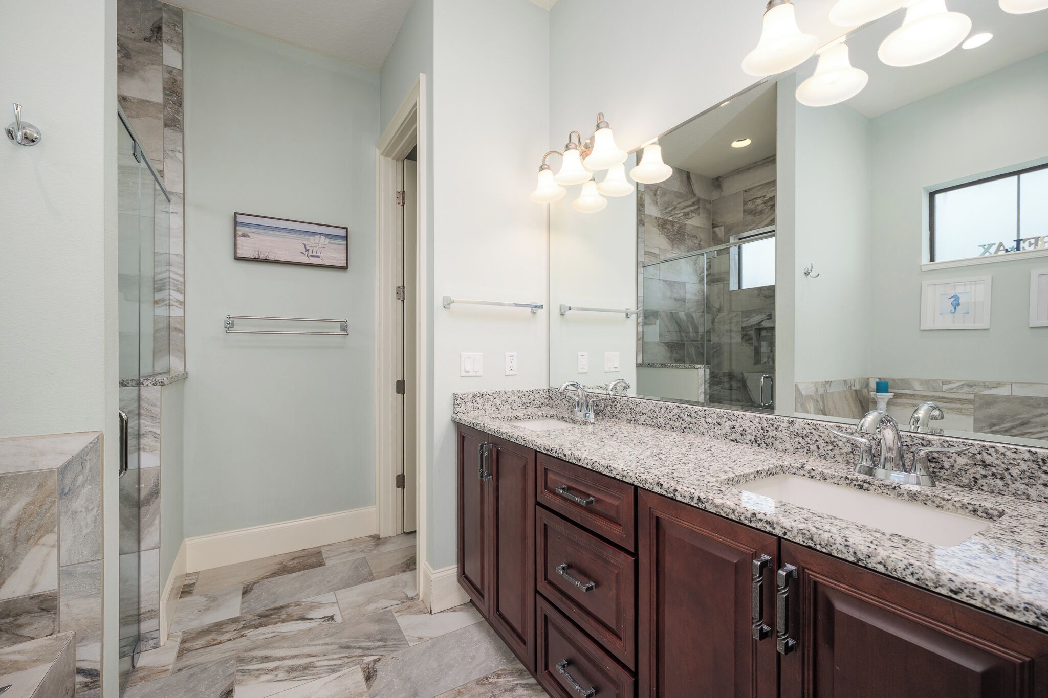 A bathroom with a granite countertop, a large mirror, and a glass shower enclosure.