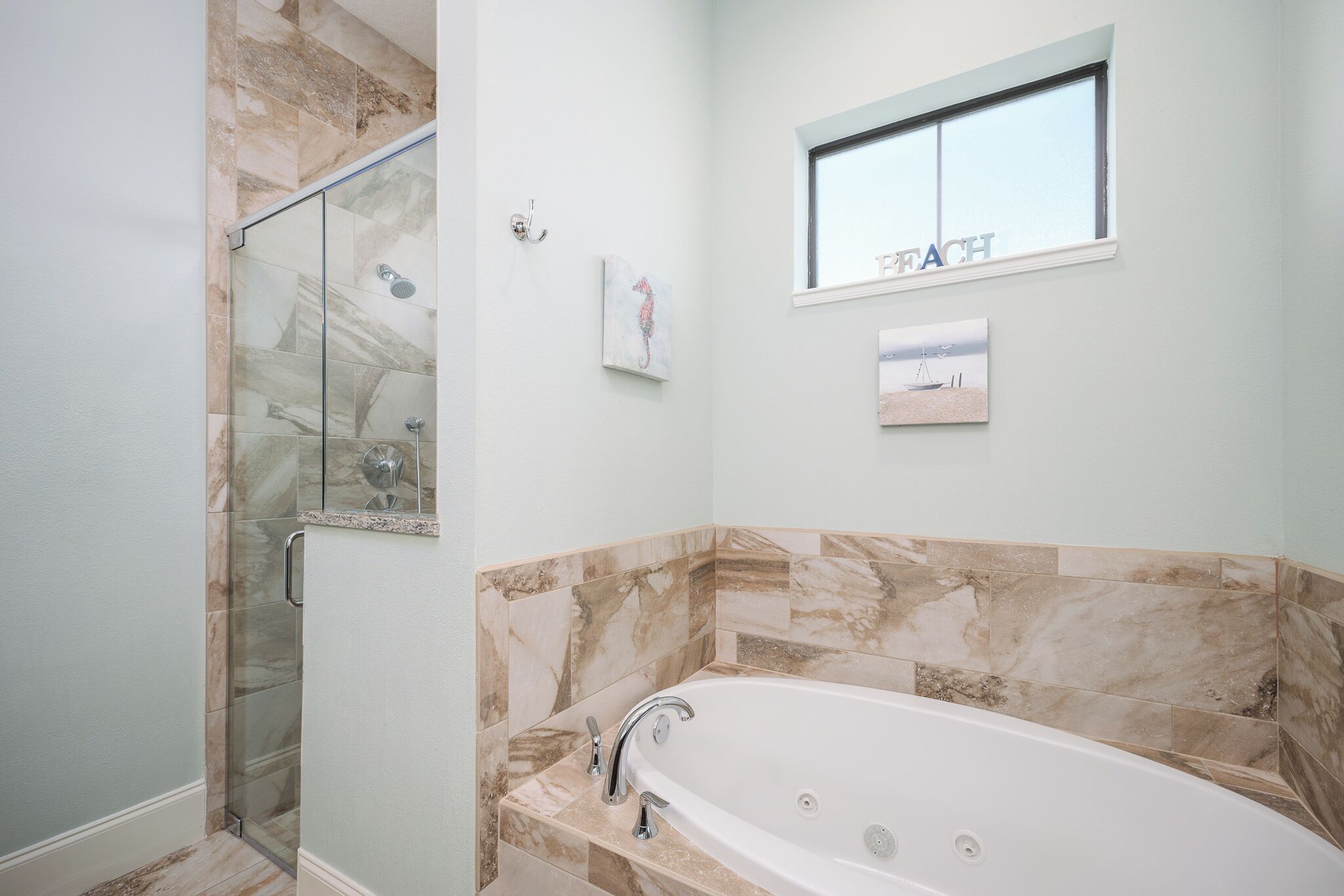 A bathroom with a glass-enclosed shower, a bathtub, and a window with a view of the beach.