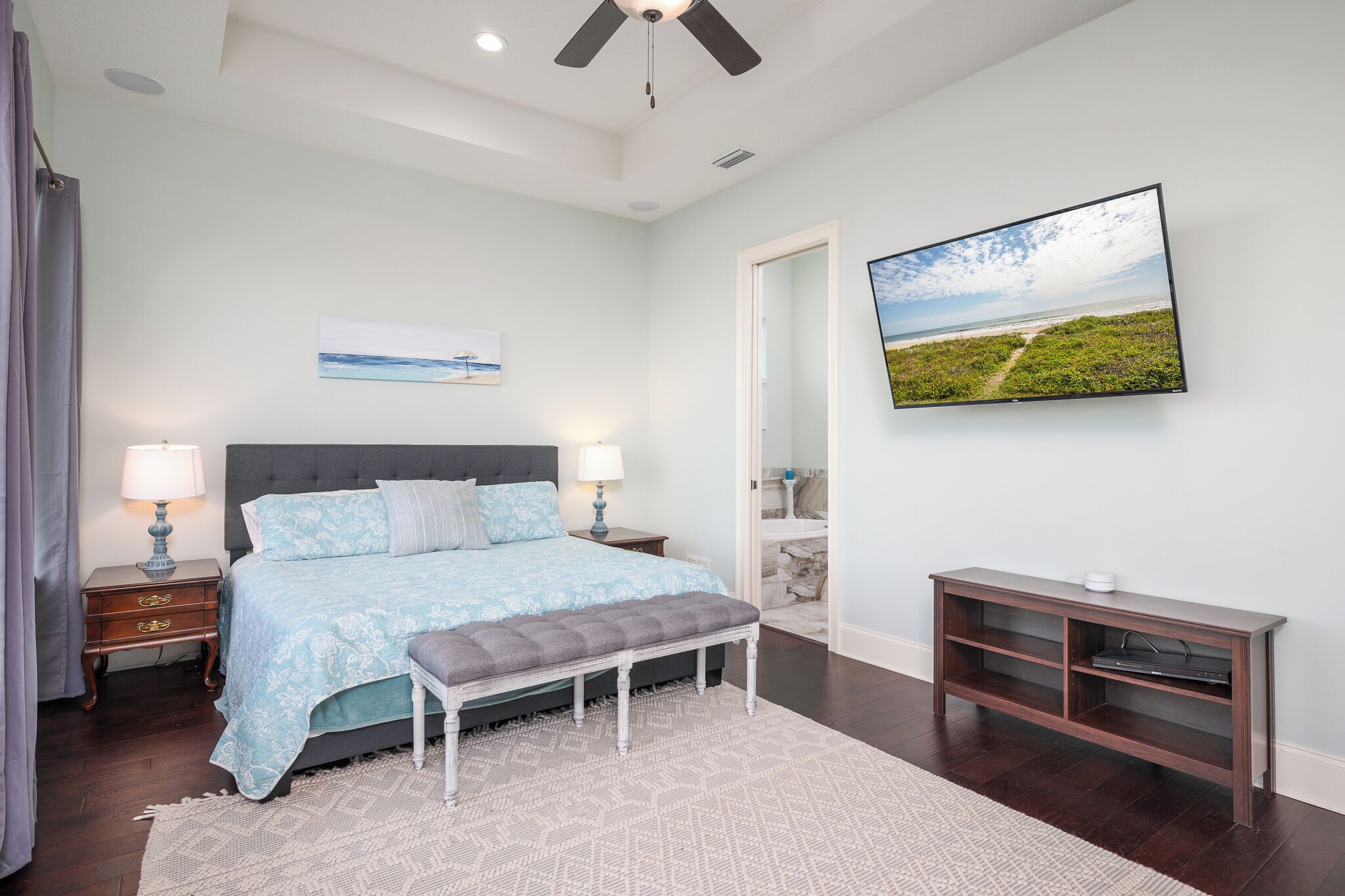 A bedroom with a bed, bedside tables, a bench, a TV, and a console table.