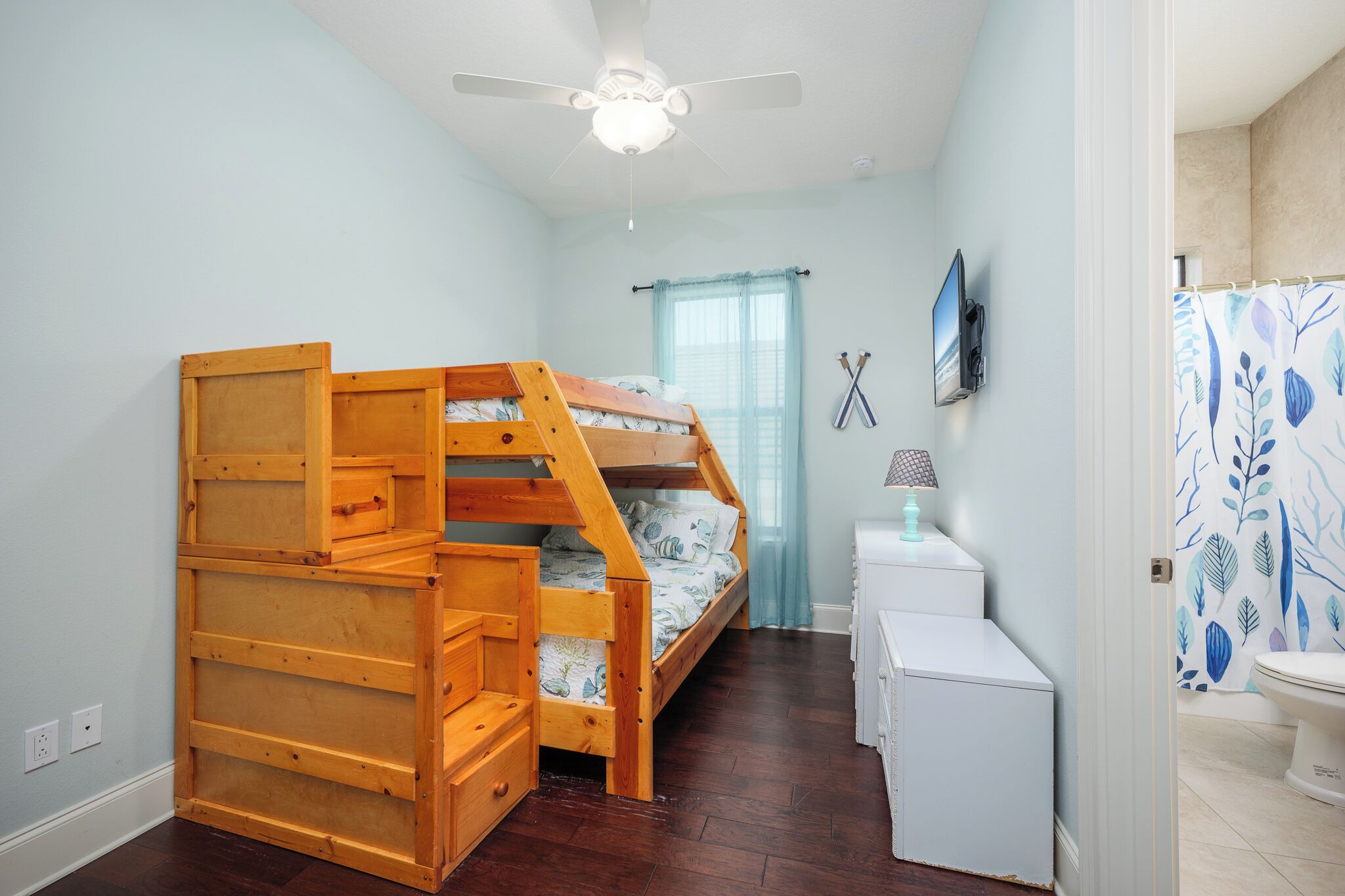 A bedroom with a bunk bed, a ceiling fan, a small white desk, and a bathroom with a shower curtain.