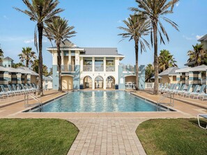 A pool area with a large pool, lounge chairs, palm trees, and a building with balconies. - Cinnamon Beach Nautilus by Distinctive Beach Rentals (Palm Coast)