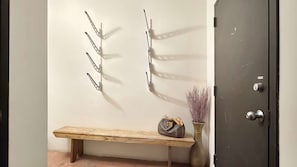 A wooden bench, a metal wall-mounted rack, and a vase with dried plants.