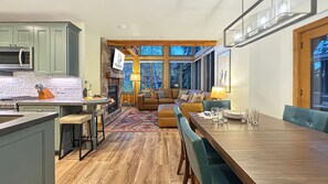 Una cocina moderna con chimenea de piedra, un comedor con mesa de madera y una sala de estar acogedora con sofá y ventana grande.