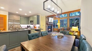 A modern kitchen with a dining area, a fireplace, and large windows.