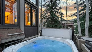 Un jacuzzi en un patio trasero con una terraza de madera y una casa al fondo.