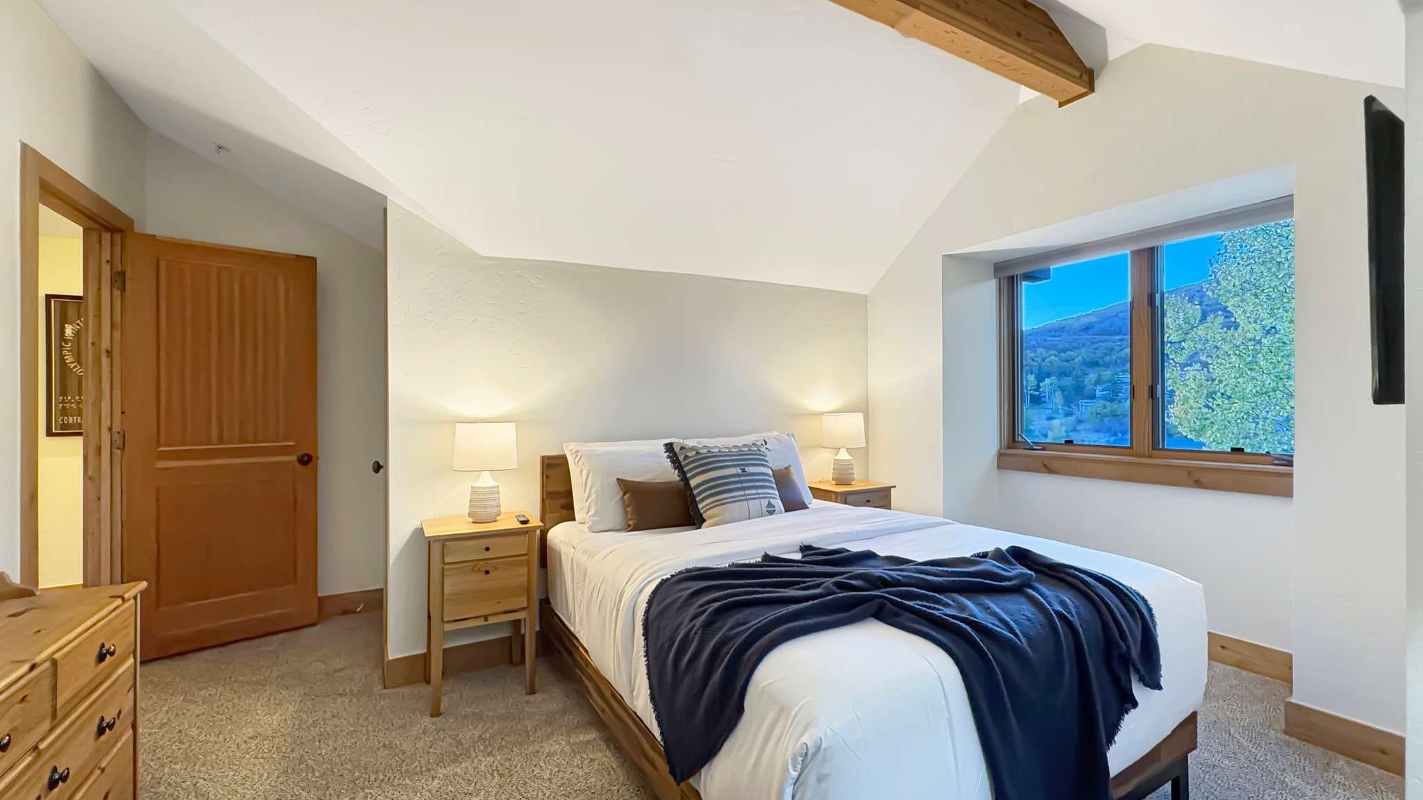 Un dormitorio con cama, mesitas de noche, armario y ventana con vistas.