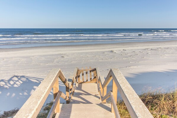 A wooden staircase leading to a beach with a clear view of the ocean.