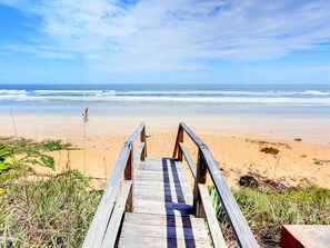 A wooden boardwalk leading to a sandy beach with the ocean in the background. - Wave Runner by Distinctive Beach Rentals (Flagler Beach)