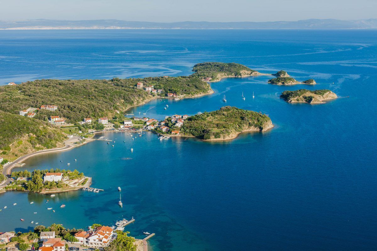 An aerial view of a coastal town with clear blue waters, several small islands, and a mix of residential and commercial buildings.
