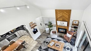 A modern living room with a fireplace, a dining area with a wooden table, and a kitchen with white cabinets.
