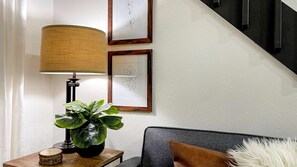 Une pièce avec une lampe, une plante en pot, un tableau encadré et un escalier.