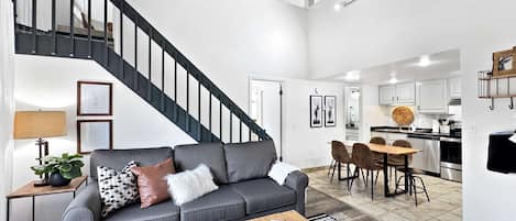 En modern inredning med en trappa, en grå soffa, en matplats och ett kök.