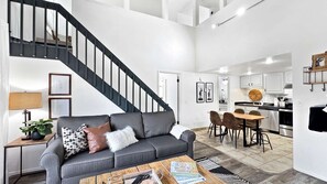 A modern interior with a staircase, a grey sofa, a dining area, and a kitchen.