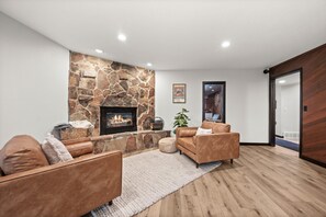 A modern living room with a stone fireplace, leather sofas, and a wooden floor. - Canyons Village Retreat•Stunning Mtn Views•Community Pools, Hot Tubs, and More (Park City)