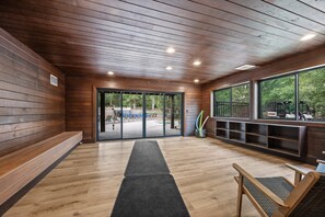 Interior de madera con un banco, una puerta que da al exterior y una ventana con vistas a la vegetación.