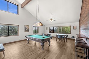 Ein Billardtisch in einem Raum mit Holzboden, großen Fenstern und einem Deckenventilator.