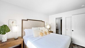 A hotel room with a bed, nightstands, a potted plant, and a door.