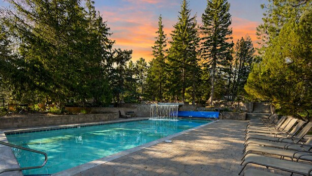 Una piscina con cascata, circondata da alberi e lettini.