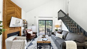 A spacious living room with a fireplace, a staircase, and a view of the outdoors.