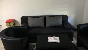 A living room with a black sofa, two grey cushions, a small table with a cup, and a painting of a bridge on the wall. - Welcome to the North Sea! 🏖️ (Cuxhaven)