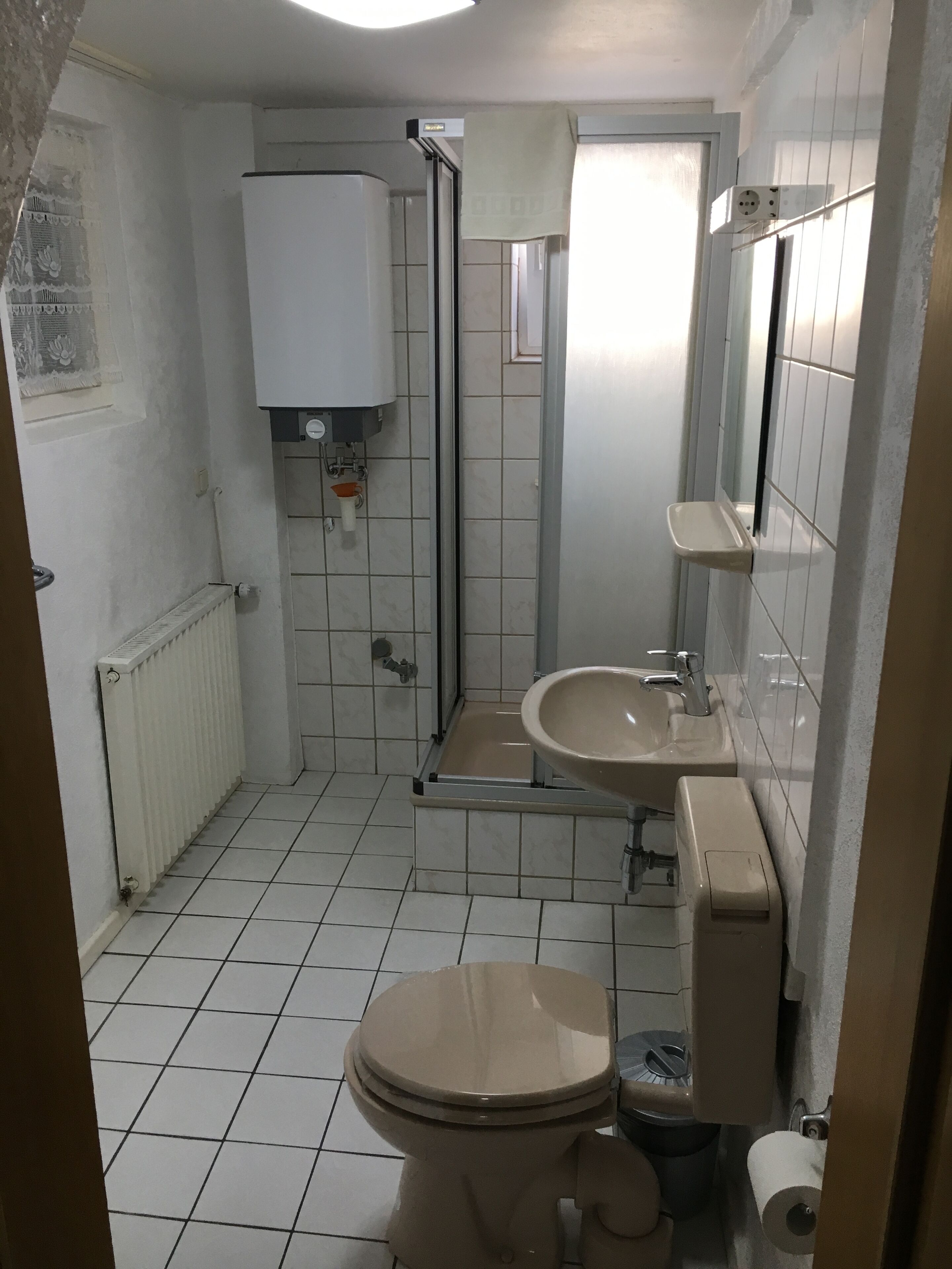 A small, tiled bathroom with a toilet, sink, and shower.