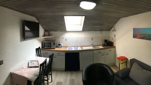 A compact kitchen with a microwave, stove, and sink. There's a dining table with chairs and a small sofa. A painting of the Golden Gate Bridge is on the wall. - Welcome to the North Sea! 🏖️ (Cuxhaven)