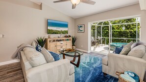 A living room with a ceiling fan, a glass coffee table, and a sofa. There is a large window with a view of greenery outside. - THE WAVES HOUSE! 7 minute walk to the beach, 2 minute walk to the JW Marriott   (Marco Island)