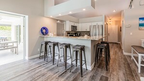 A modern kitchen with a central island, bar stools, and a dining area with a bench. - THE WAVES HOUSE! 7 minute walk to the beach, 2 minute walk to the JW Marriott   (Marco Island)