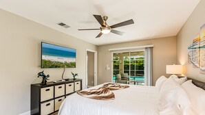 A bedroom with a bed, a ceiling fan, a TV, a dresser, and a view of a pool. - THE WAVES HOUSE! 7 minute walk to the beach, 2 minute walk to the JW Marriott   (Marco Island)