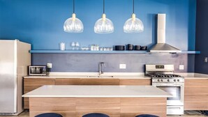 Une cuisine moderne dotée d’un îlot central, de meubles en bois, d’un réfrigérateur en acier inoxydable, d’un four à micro-ondes, d’une cuisinière et de luminaires suspendus.