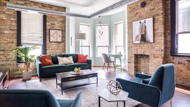 Un salon moderne avec un mur en briques, un canapé vert, une table basse et un fauteuil bleu.