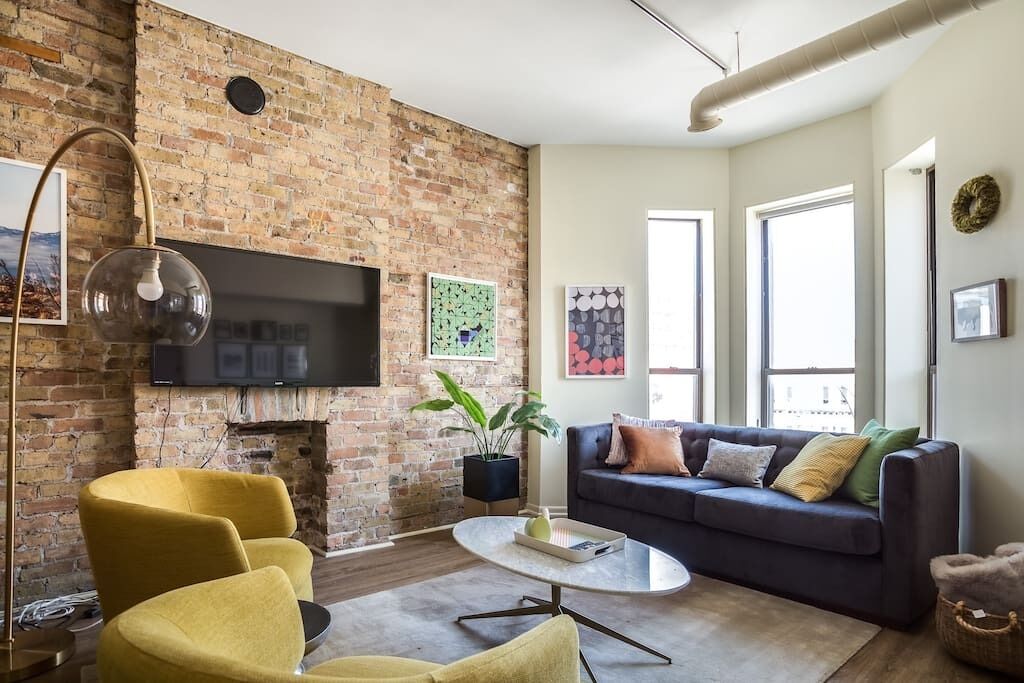 A living room with a brick wall, a flat-screen TV, a sofa, and a coffee table.